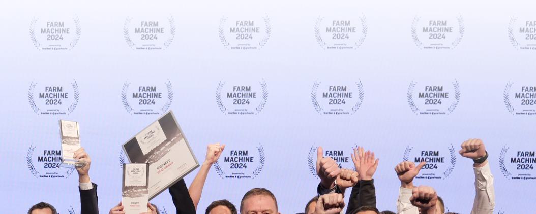 Vor einer weißen Leinwand, auf der in regelmäßigen Abständen das Logo des Farm Machine-Awards zu sehen ist, sind in der unteren Bildhälfte die Arme von jubelnden Menschen zu sehen. Manche halten Urkunden und Pokale.  