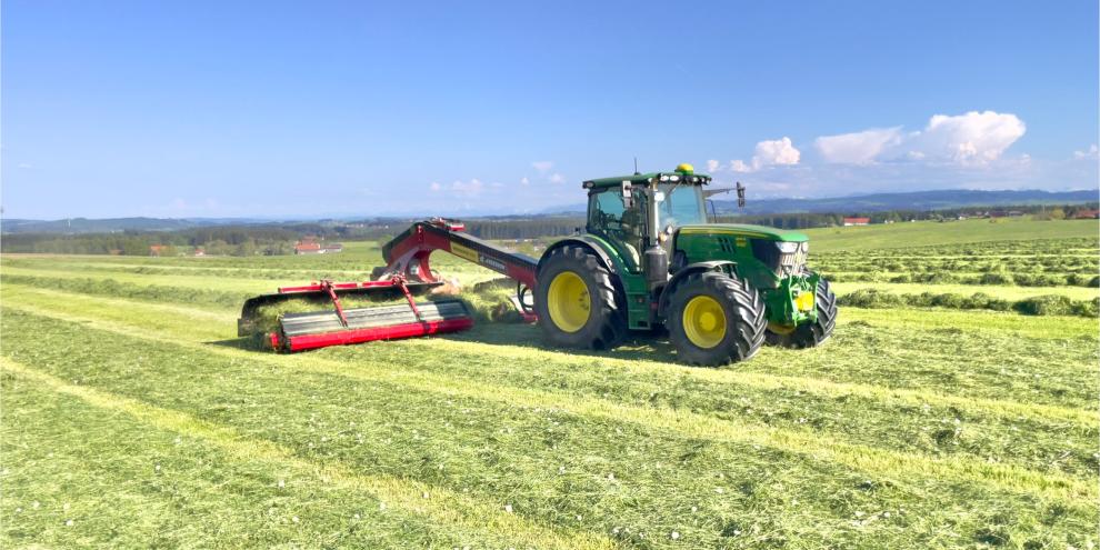 Traktor mit Bandschwader auf einer Wiese.
