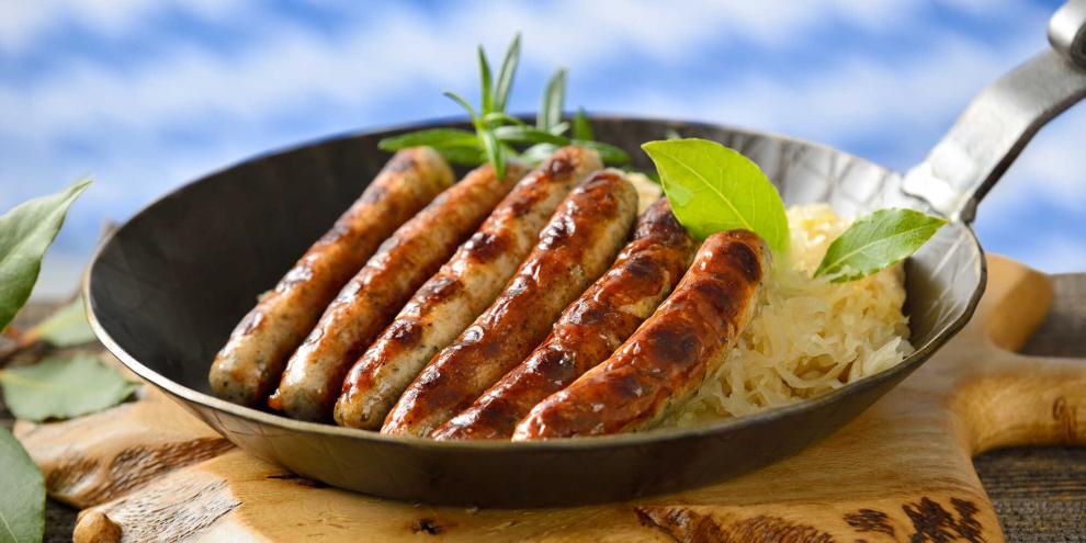 Eine Eisenpfannne voller Nürnberger Rostbratwürste auf Sauerkraut.