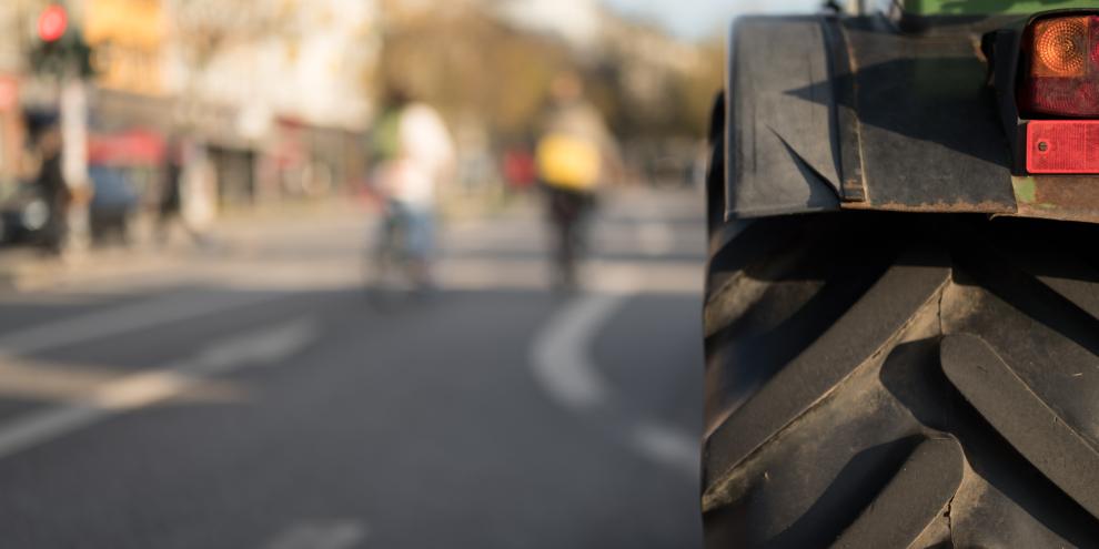 Traktor fährt auf einer Straße. Nebenan sind Fahrradfahrer zu erkennen. Sicherheit im Straßenverkehr ist für Traktoren ein wichtiges Thema.