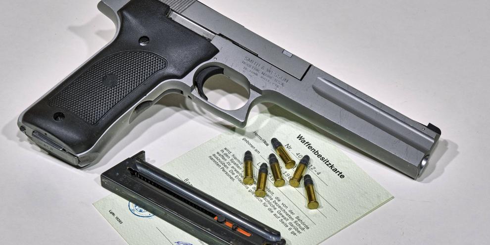 Sportpistole liegt neben Munition auf einer grünen Waffenbesitzkarte