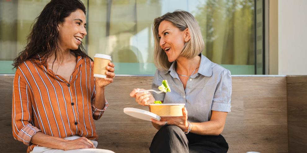 Zwei Geschäftsfrauen beim freundschaftlichen Mittagessen im Freien. Sie essen Salat und trinken Kaffee.