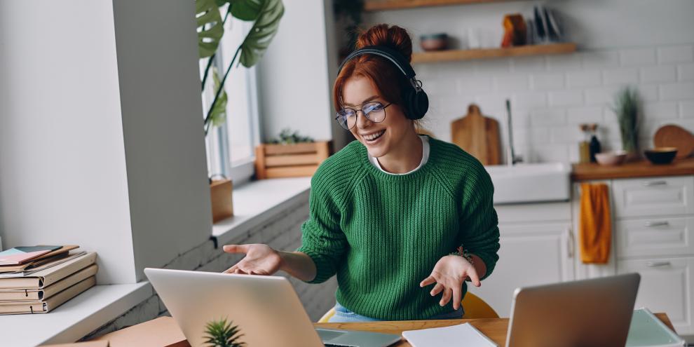 Fröhliche junge Frau mit Kopfhörern nimmt während der Arbeit im Homeoffice an einer Webkonferenz teil.