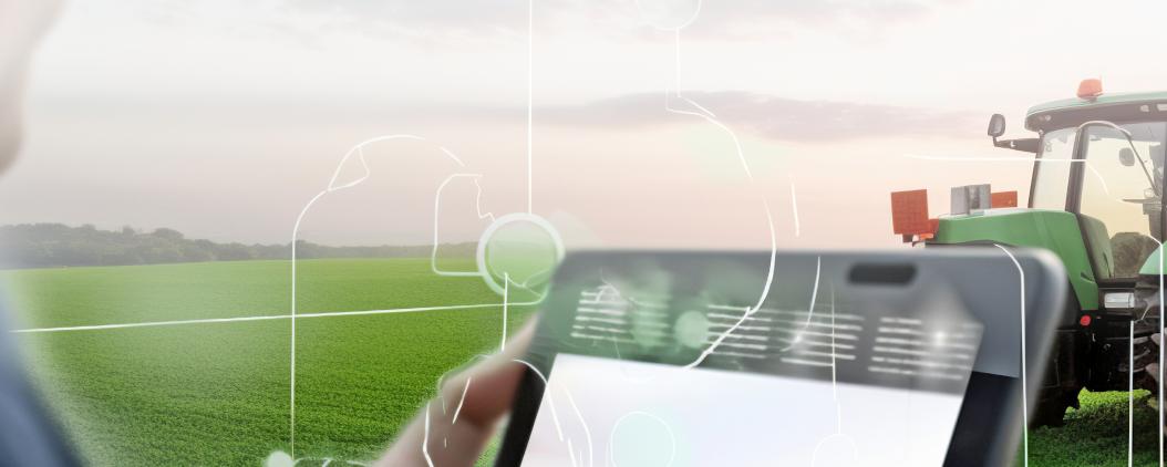 Auf einem Feld steht ein Landwirt vor seinem Trecker und nutzt mit einem Tablet eine Planungssoftware. 