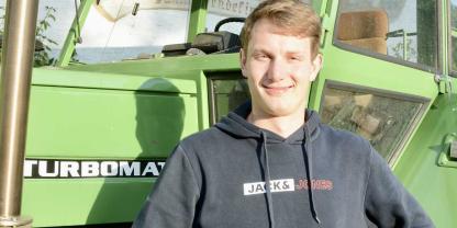 Porträt des jungen Mannes vor einem Traktor. 