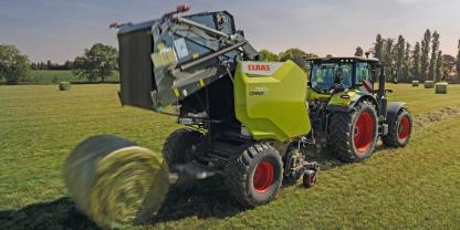Traktor mit Rundballenpresse arbeitet auf einer Wiese.