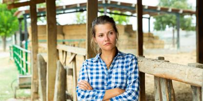Eine Landwirt lehnt mit niedergeschlagenem Blick am Stall.