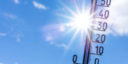Thermometer vor blauem Himmel und Sonne
