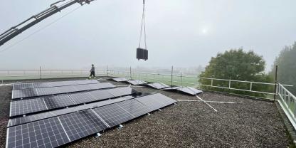 Ein Kran hebt die faltbare PV-Anlage SmartSolarBox auf das Dach. Dort muss sie nur noch auseinandergeklappt werden.