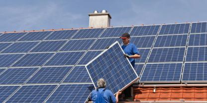 Zwei Handwerker installieren eine PV-Anlage auf einem hausdach. Doch wie viel kWp muss man installieren, um genügend kWh zu erzeugen?