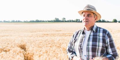 Ein älterer Landwirt steht in einem Getreidefeld und schaut skeptisch.