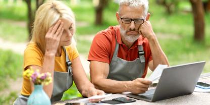 Ein älteres Paar sitzt im Garten und blickt kritisch auf einen Laptop.