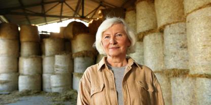 Eine ältere Landwirtin steht in einer Halle mit Rundballen.