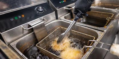 Ein koch frittiert Lebensmittel in Speisefett.