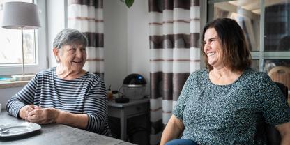 Mutter Ruth und Tochter Claudia sitzen am Esstisch und lächeln sich an.