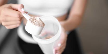 Eine Frau löffelt Eiweißpulver aus einem Becher.