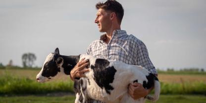 Ein Landwirt hält ein Kalb auf dem Arm, das aufgrund geschwächter Beine nicht laufen kann (Symbolbild).