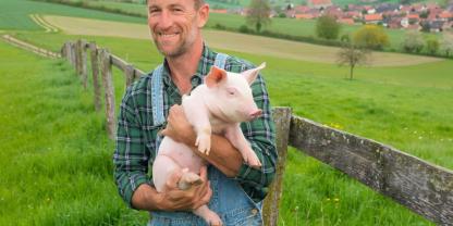 Ein schönes Bild von einem Landwirt mit Ferkel auf der grünen Wiese – die KI macht es möglich. Unser Kolumnisten Sabine Schrauth fragt sich allerdings, ob solche schönen, aber unrealistischen Bilder der Landwirtschaft wirklich helfen.