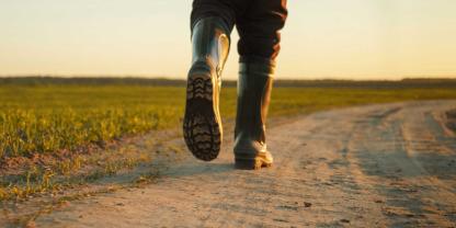 Ein Landwirt mit Gummistiefeln auf einem Feldweg