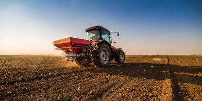 Ein Landwirt bringt Dünger aus mit dem Traktor und einem Düngerstreuer.