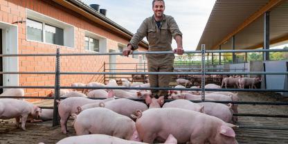 Ein junger Landwirt steht im Auslauf seiner Schweine und blickt in die Kamera.