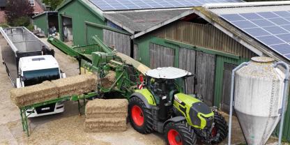 Ein Claas Axion 9.450 Traktor mit einer Krone Premos 5000 auf einem Bauernhof