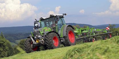 Ein Traktor mit Schwader am Hang: Unebener Untergrund, Gefälle und das Anbaugerät beeinflussen, wie kippsicher die Maschine bleibt.