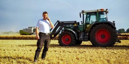 Ein Landwirt steht mit dem Handy in der Getreideernte auf dem Feld.