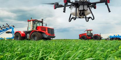 DJI-Agrardrohne fliegt über einen Acker, im Hintergrund sind Traktoren zu sehen.