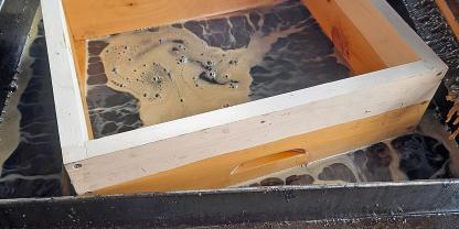 Ein Honigraum aus Holz schwimmt im heißen, flüssigen Wachs.