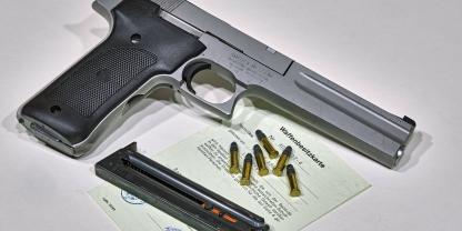 Sportpistole liegt neben Munition auf einer grünen Waffenbesitzkarte
