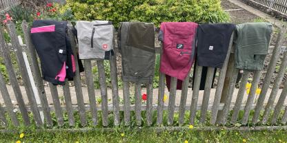 Sechs Arbeitshosen hängen über einem Gartenzaun