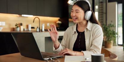 Eine Frau mit Kopfhörern winkt während eines Videoanrufs im Homeoffice