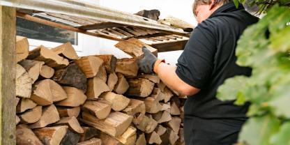 Ein Mann prüft Holzscheite auf seinem Brennholzstapel (Symbolbild). Wie erkennt man, ob das Brennholz trocken genug ist zum verfeuern?.