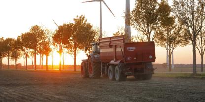 Ein Traktor mit Anhänger fährt in den Sonnenuntergang.